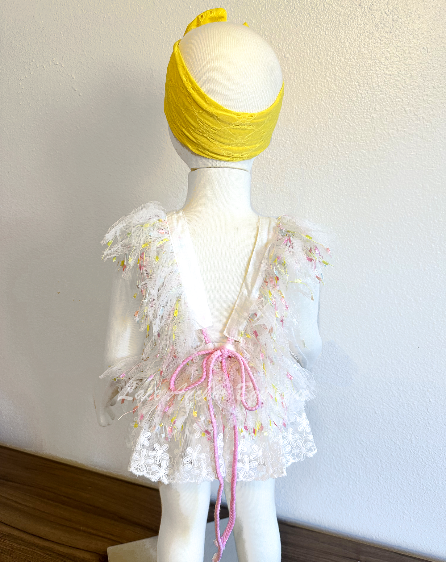 white lace baby girls romper with multi colored pastel rainbow confetti fringe, yellow, blue, and peach embroidered butterflies, and lace skirt. Baby girl first birthday smash cake outfit.