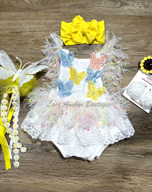 white lace baby girls romper with multi colored pastel rainbow confetti fringe, yellow, blue, and peach embroidered butterflies, and lace skirt. Baby girl first birthday smash cake outfit. 