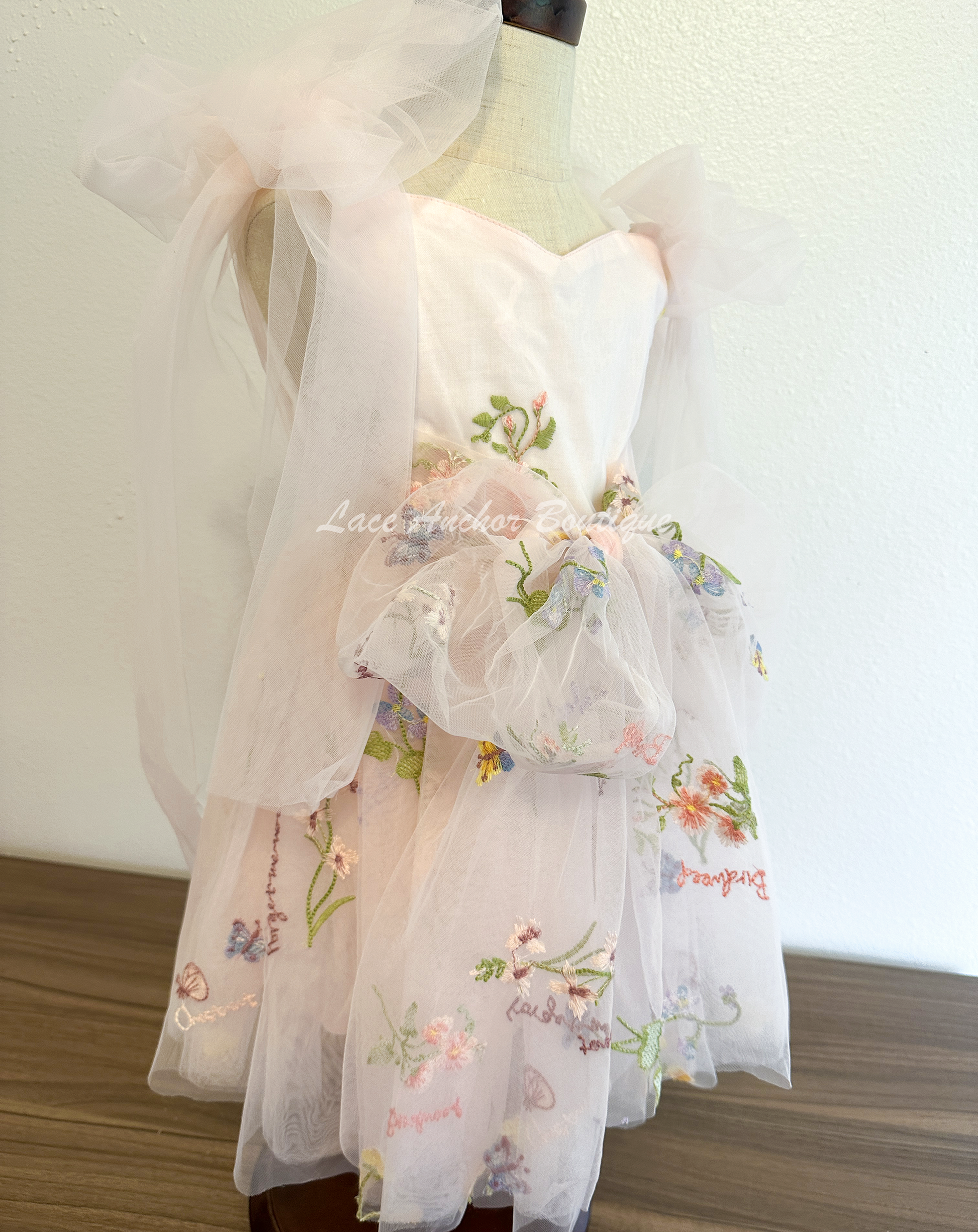 toddler youth puffy tied shoulder flower girl dress with large tied bow tied at waist. Outfits in light blush pink with emboridered floral print.