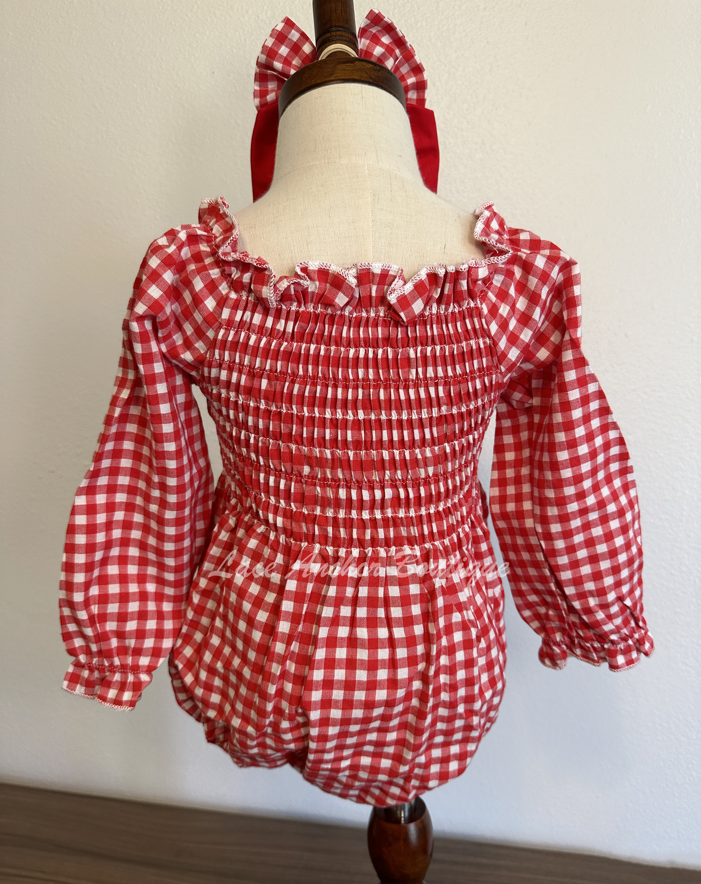 red and white gingham print long sleeve baby girls romper with smocked top and large red sailor bow on chest. Comes with matching bow on nylon band.