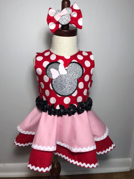 baby girls minnie mouse themed red polka dotted dress dress with red and pick double layer skirt with ric rack trim, silver sparkle mouse head with bow, black flowers around waist, and matching hair bow. 