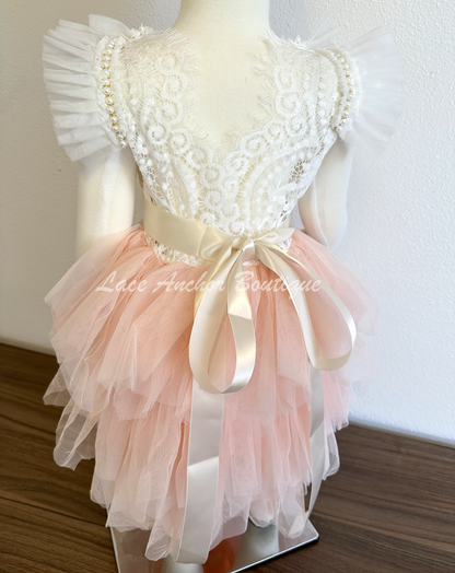 lace and tulle flower girls dress. white lace top with ruffled tulle sleeves and beaded pearl and rhinestone detailing with blush pink layered tulle skirt and silk flower tied sash.