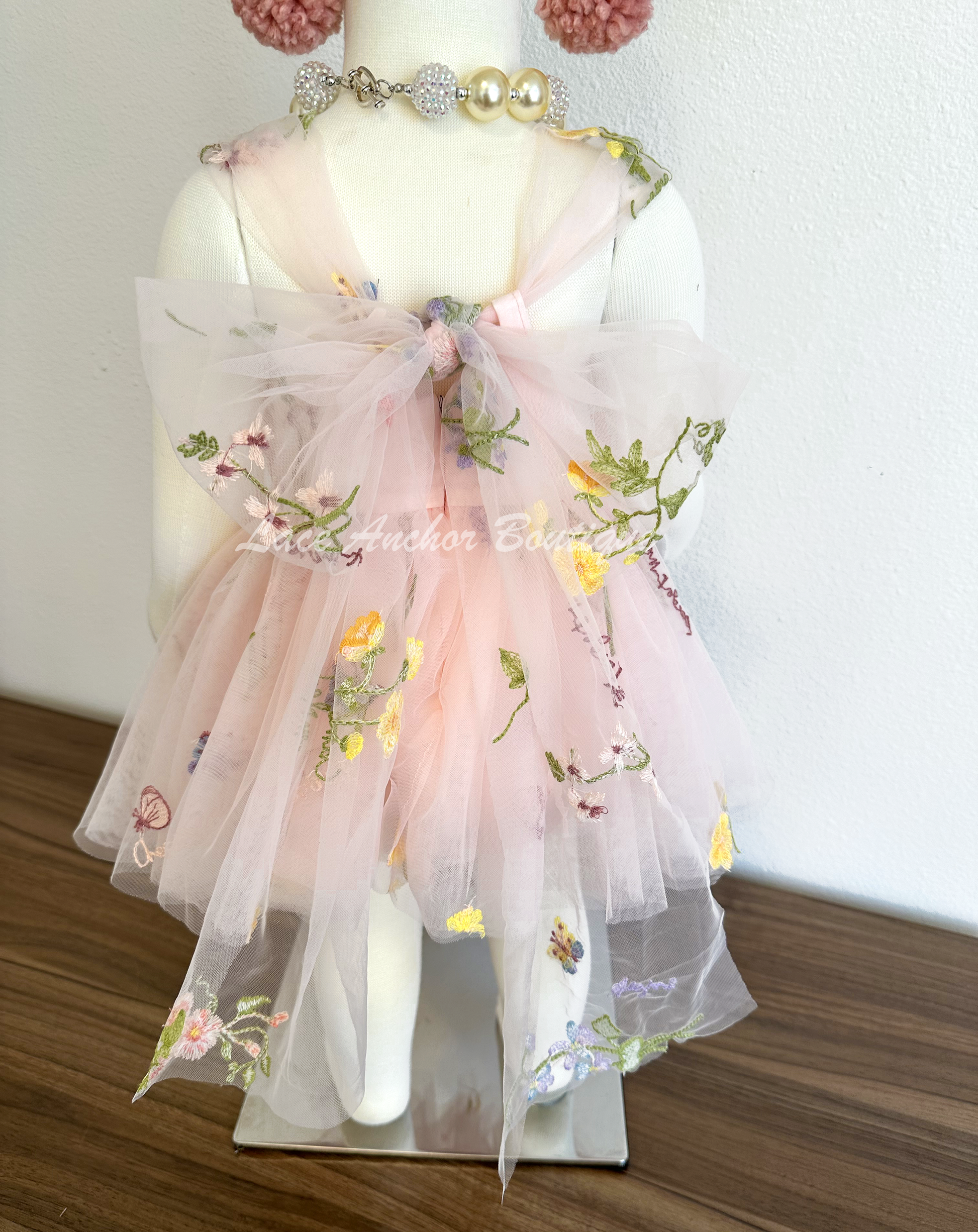 Baby girls romper with tied back fluffy bow. Outfits in light blush pink with embroidered floral print.