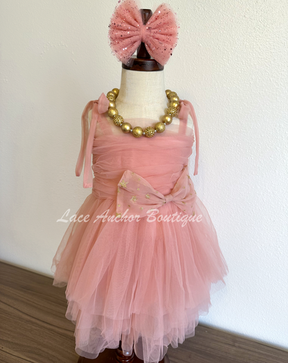 mauve rose pink girls dress with large bow in gold glitter star print witj rouched top and tied bow shoulder. Layered skirt.