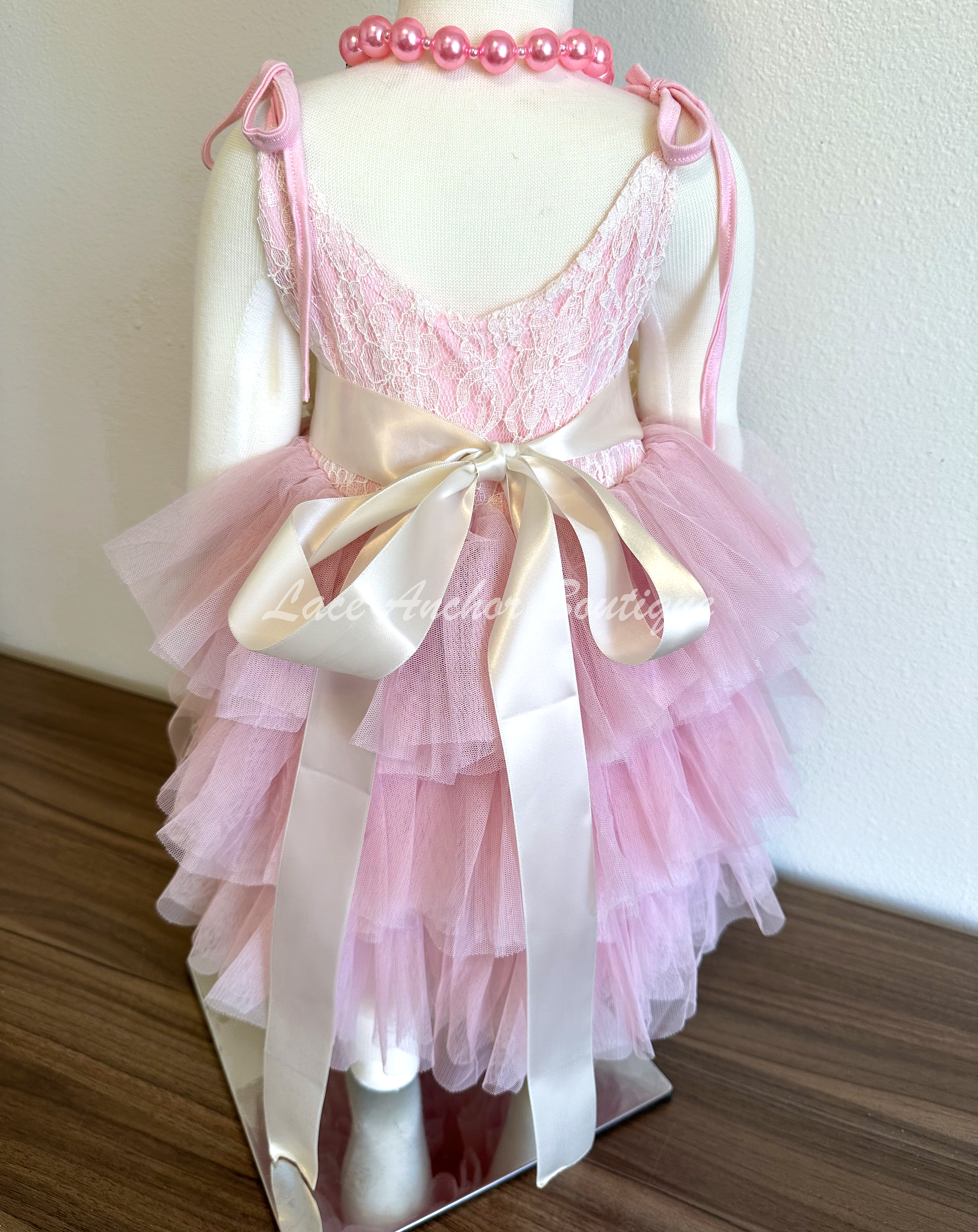 Light pink toddler girls dress with lace top, tied straps, layered ruffled tulle skirt, and silky floral tied sash. Girls flower girl dress.