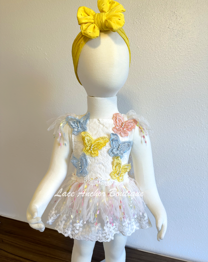 white lace baby girls romper with multi colored pastel rainbow confetti fringe, yellow, blue, and peach embroidered butterflies, and lace skirt. Baby girl first birthday smash cake outfit.