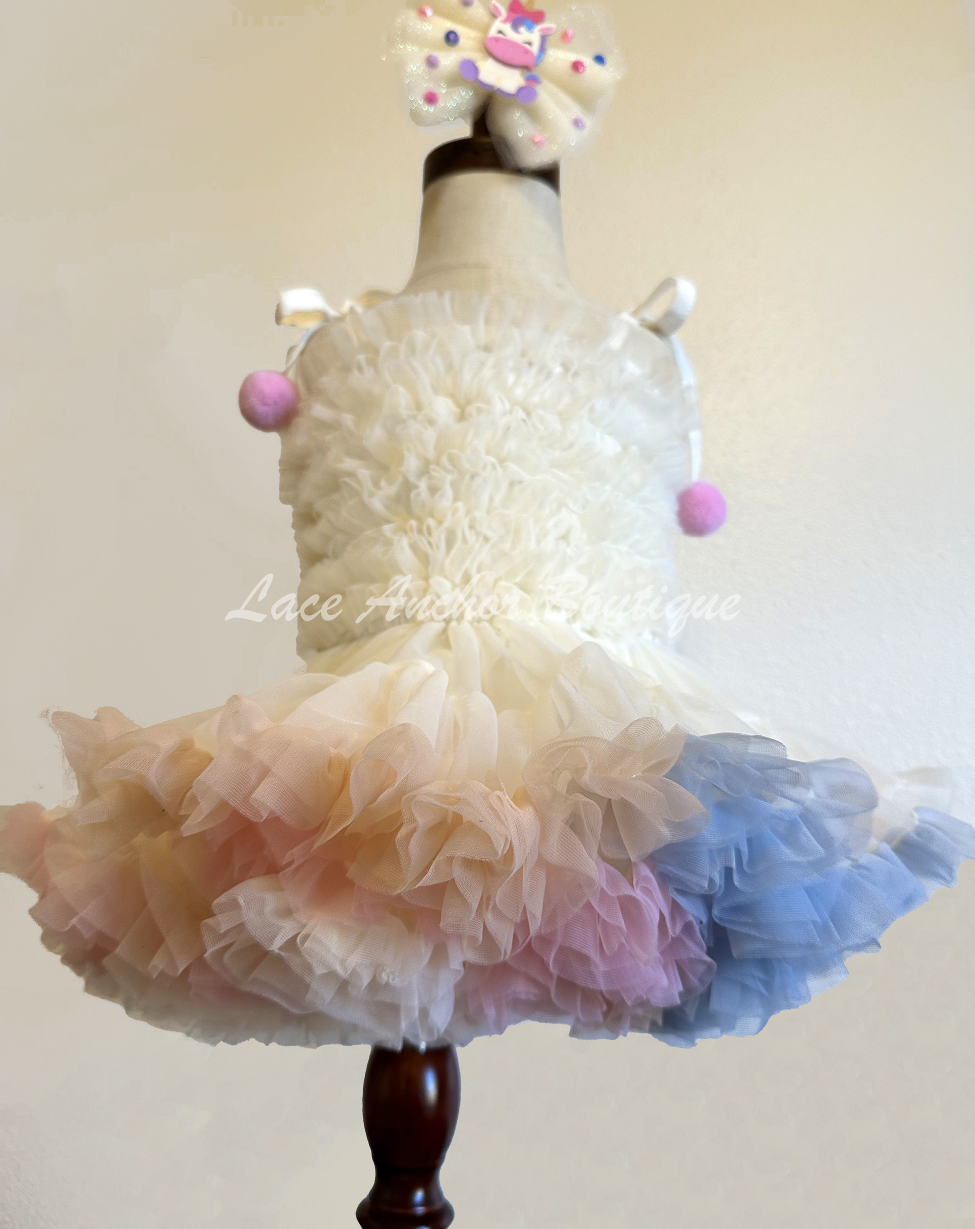 toddler baby girls pastel rainbow multi colored dress with pearl details, smocked ruffle top, and ruffle trim and tied pom pom straps. Unicorn colored theme birthday girl princess dress.
