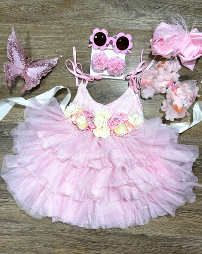 Light pink toddler girls dress with lace top, tied straps, layered ruffled tulle skirt, and silky floral tied sash. Girls flower girl dress.