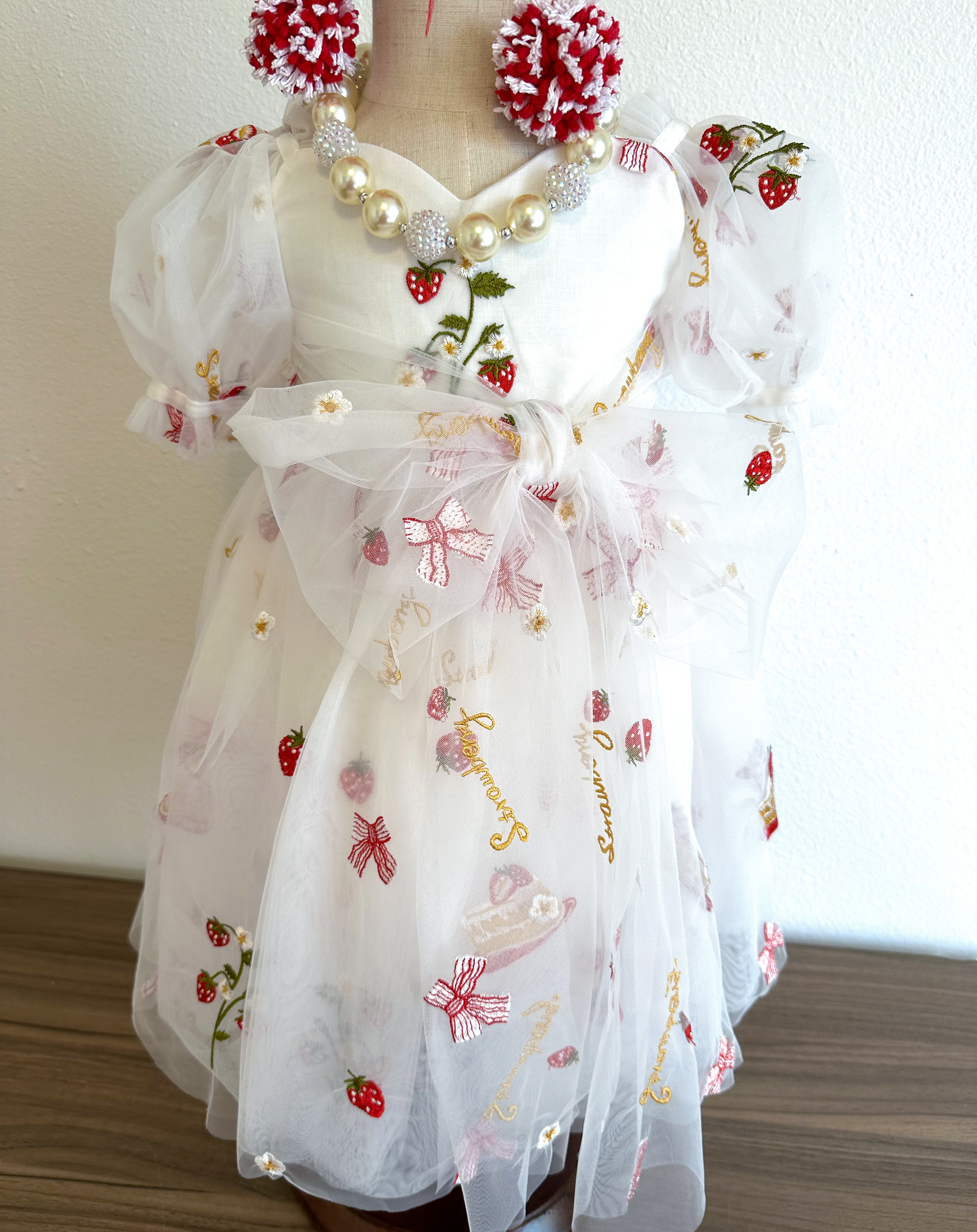 white dress with strawberries, bows, and strawberry shortcake embroidered print with large fluffy tied bow and puff sleeves.