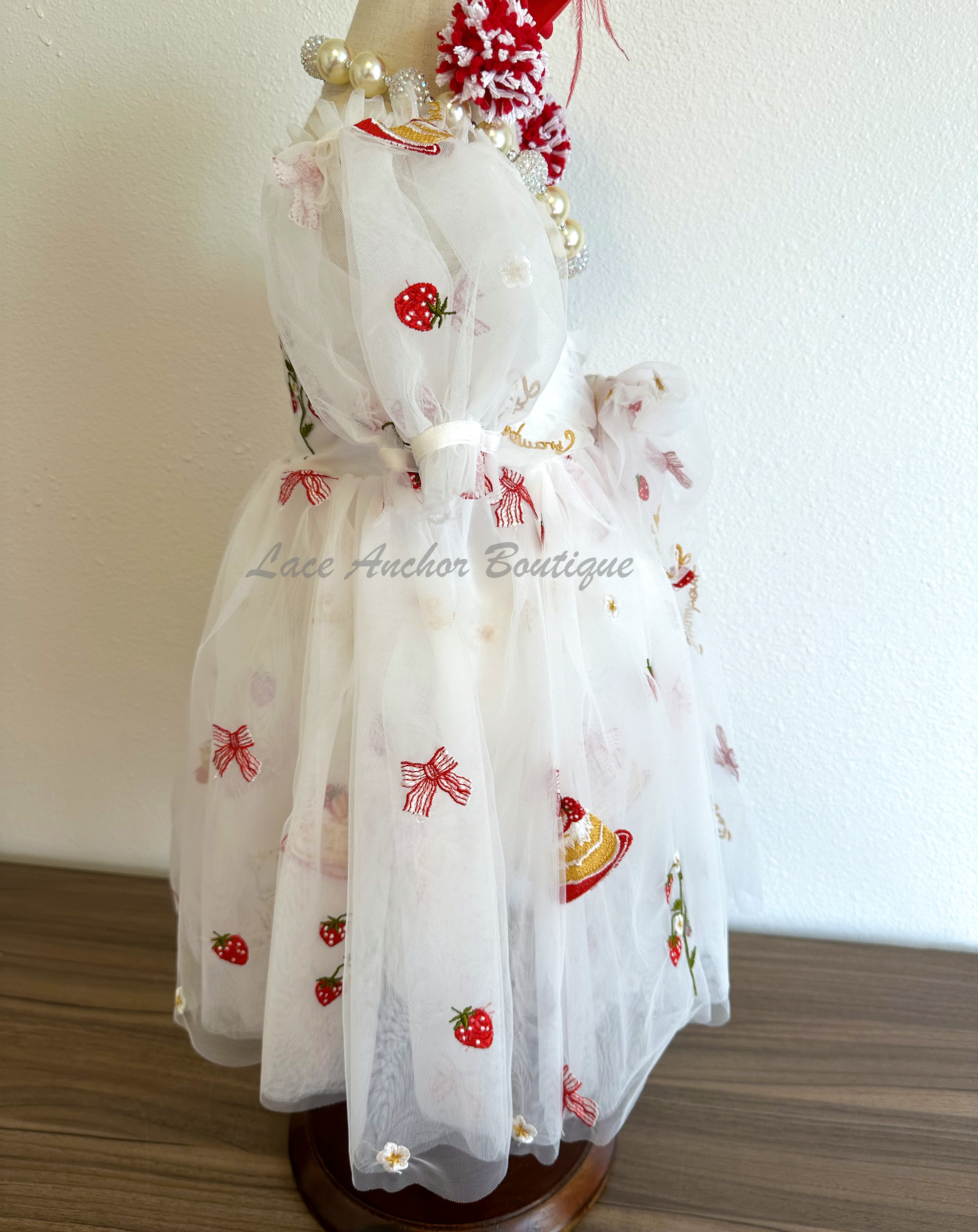 white dress with strawberries, bows, and strawberry shortcake embroidered print with large fluffy tied bow and puff sleeves.