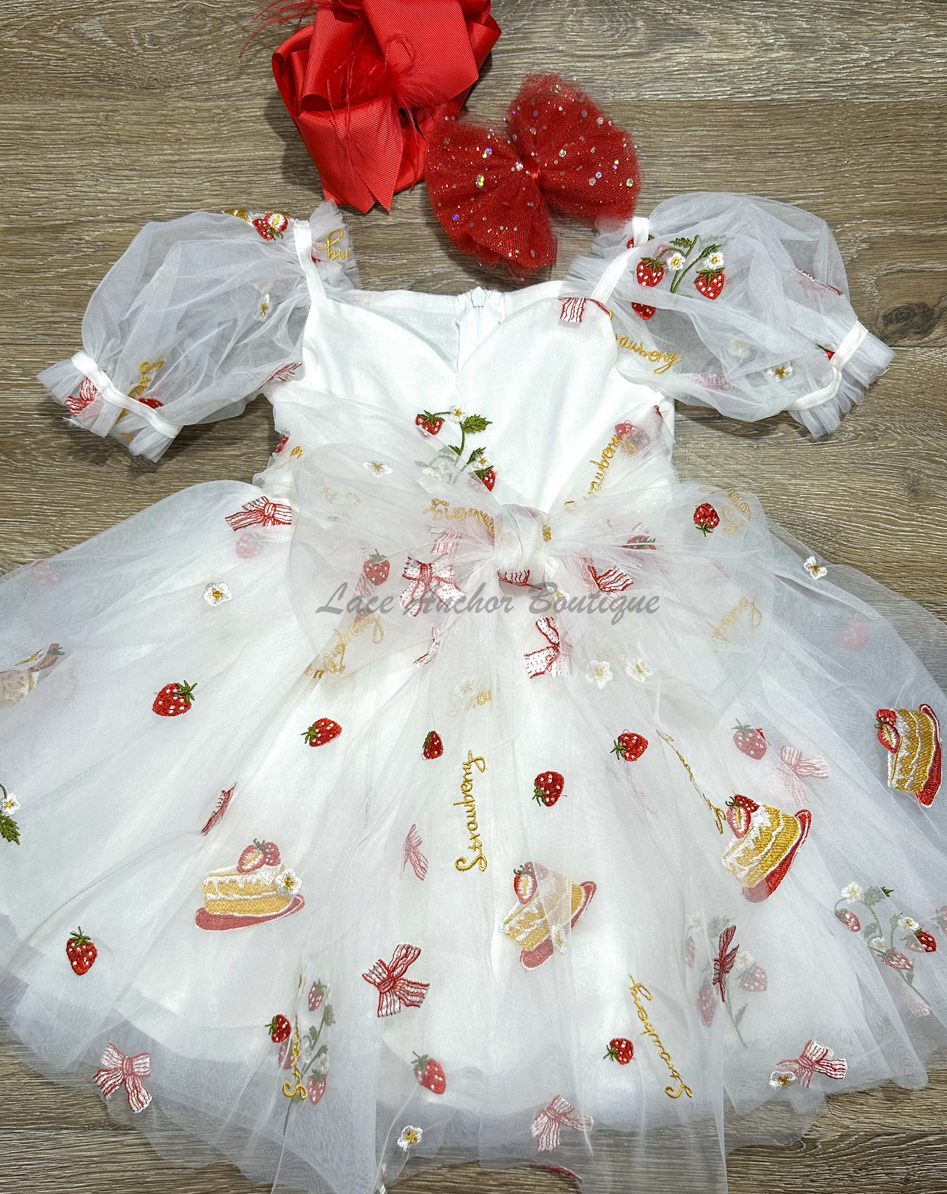 white dress with strawberries, bows, and strawberry shortcake embroidered print with large fluffy tied bow and puff sleeves.