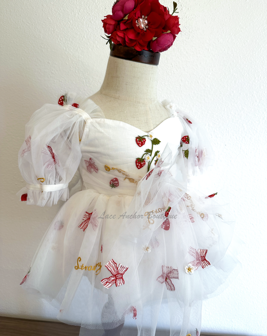 white romper with strawberries, bows, and strawberry shortcake embroidered print with large fluffy tied bow and puff sleeves.