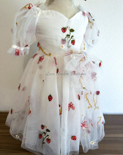 white dress with strawberries, bows, and strawberry shortcake embroidered print with large fluffy tied bow and puff sleeves.