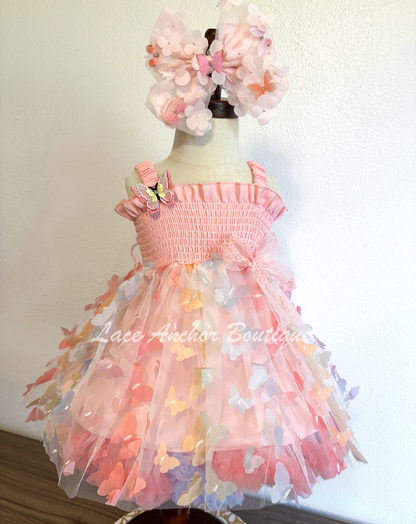 Light blush pale pink rainbow girls butterfly wing fairy dress in pink on model child toddler. Has butterflies all over skirt.