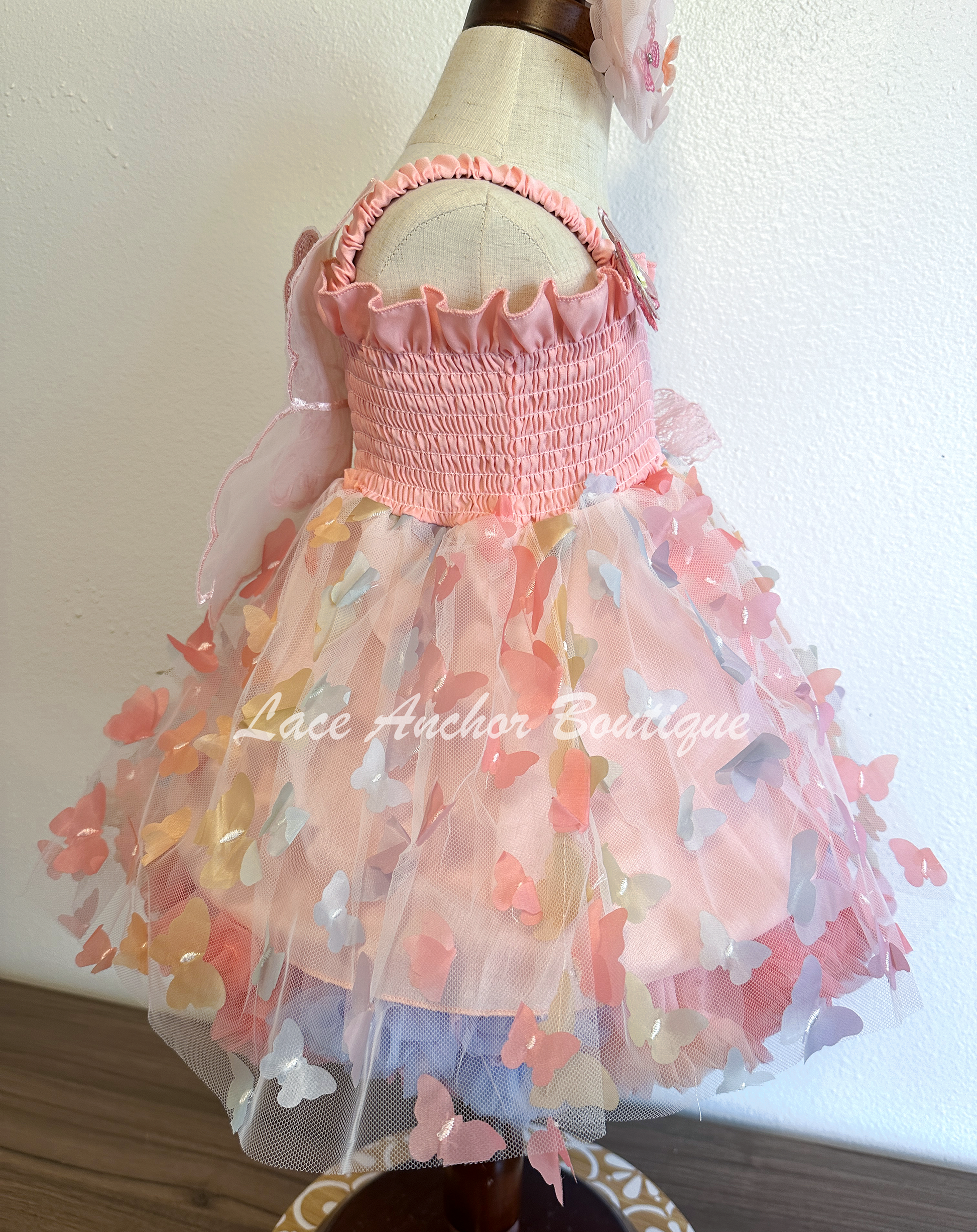 Light blush pale pink rainbow girls butterfly wing fairy dress in pink on model child toddler. Has butterflies all over skirt.