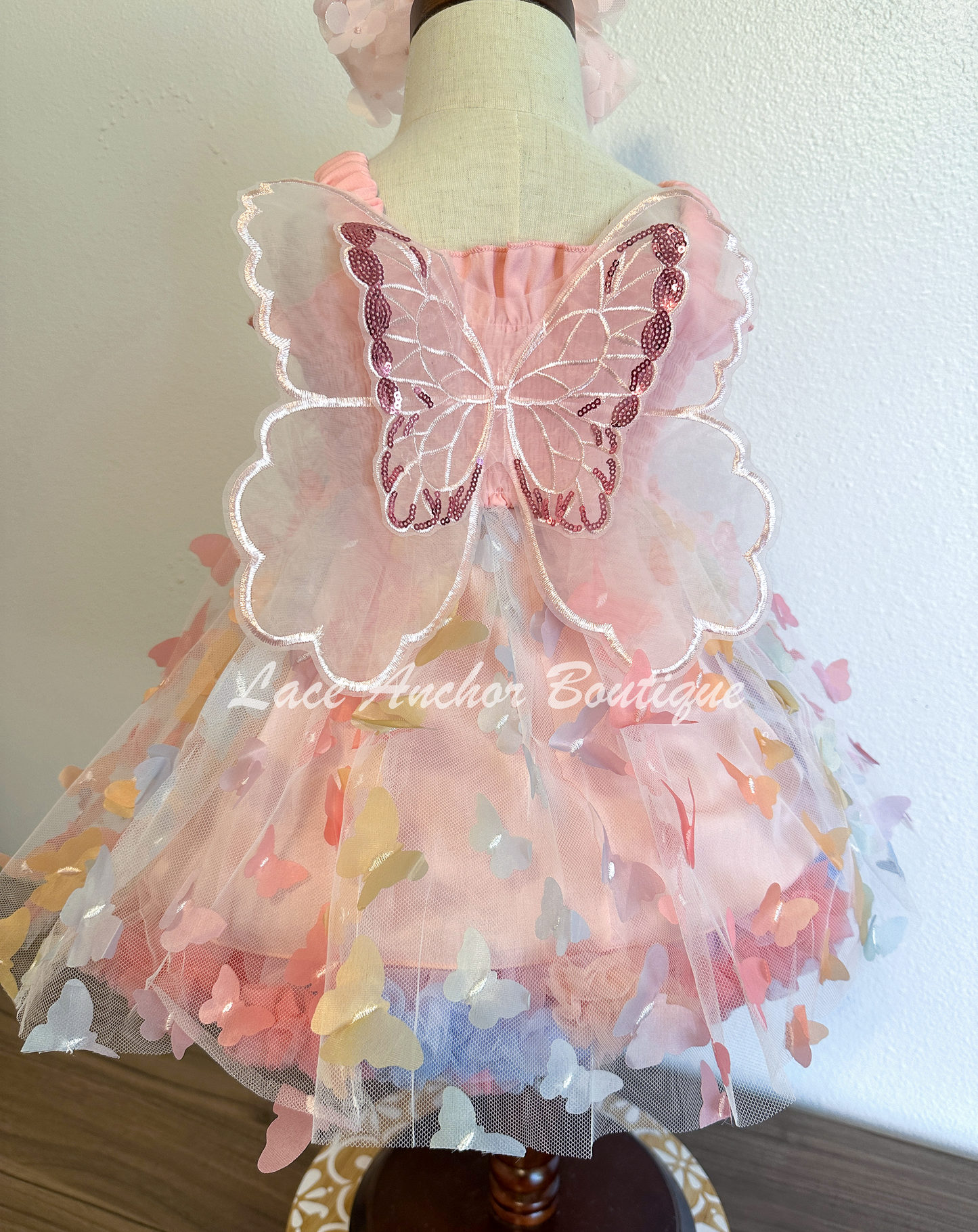 Light blush pale pink rainbow girls butterfly wing fairy dress in pink on model child toddler. Has butterflies all over skirt.