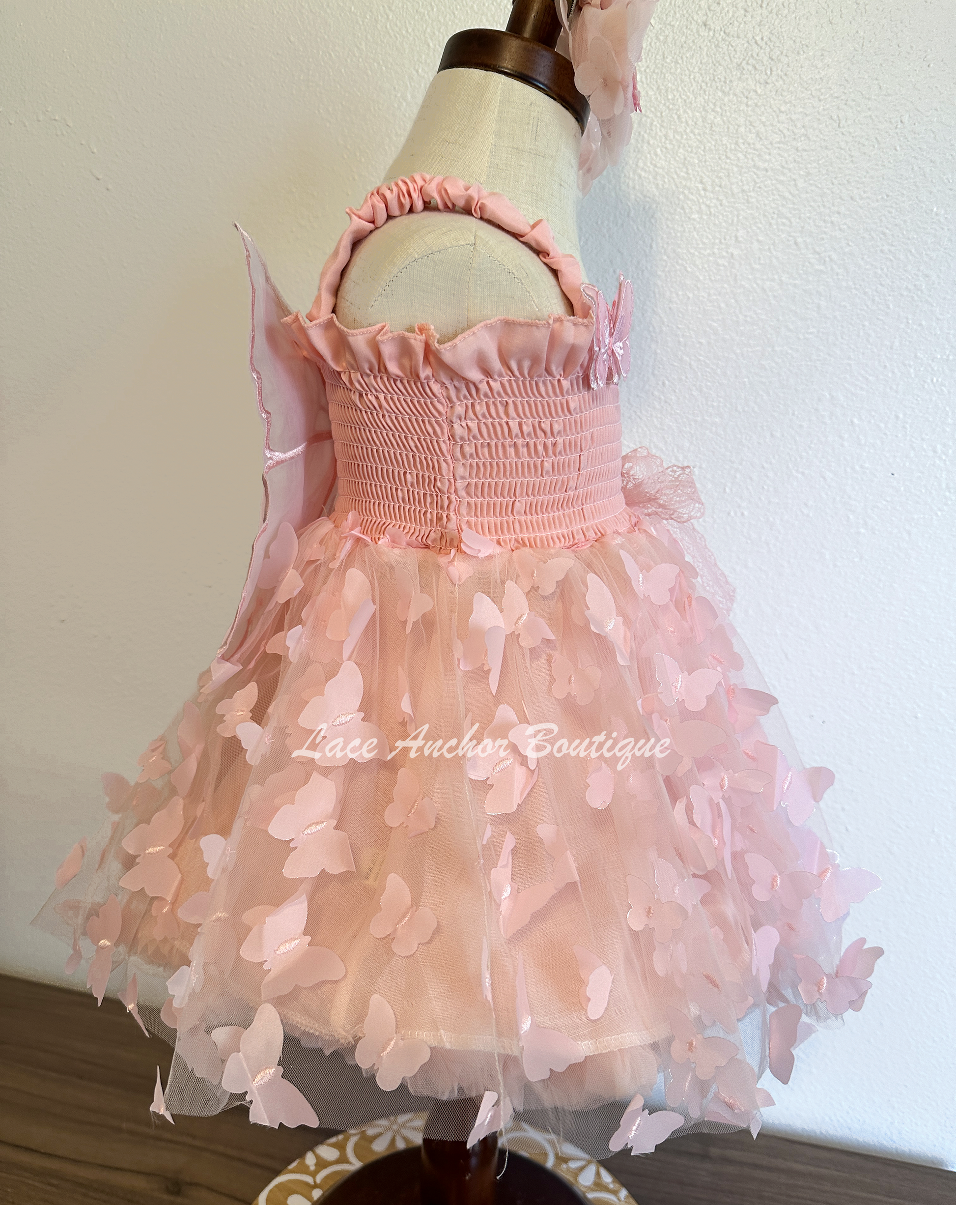 Light blush pale pink girls butterfly wing fairy dress in pink on model child toddler. Has butterflies all over skirt.