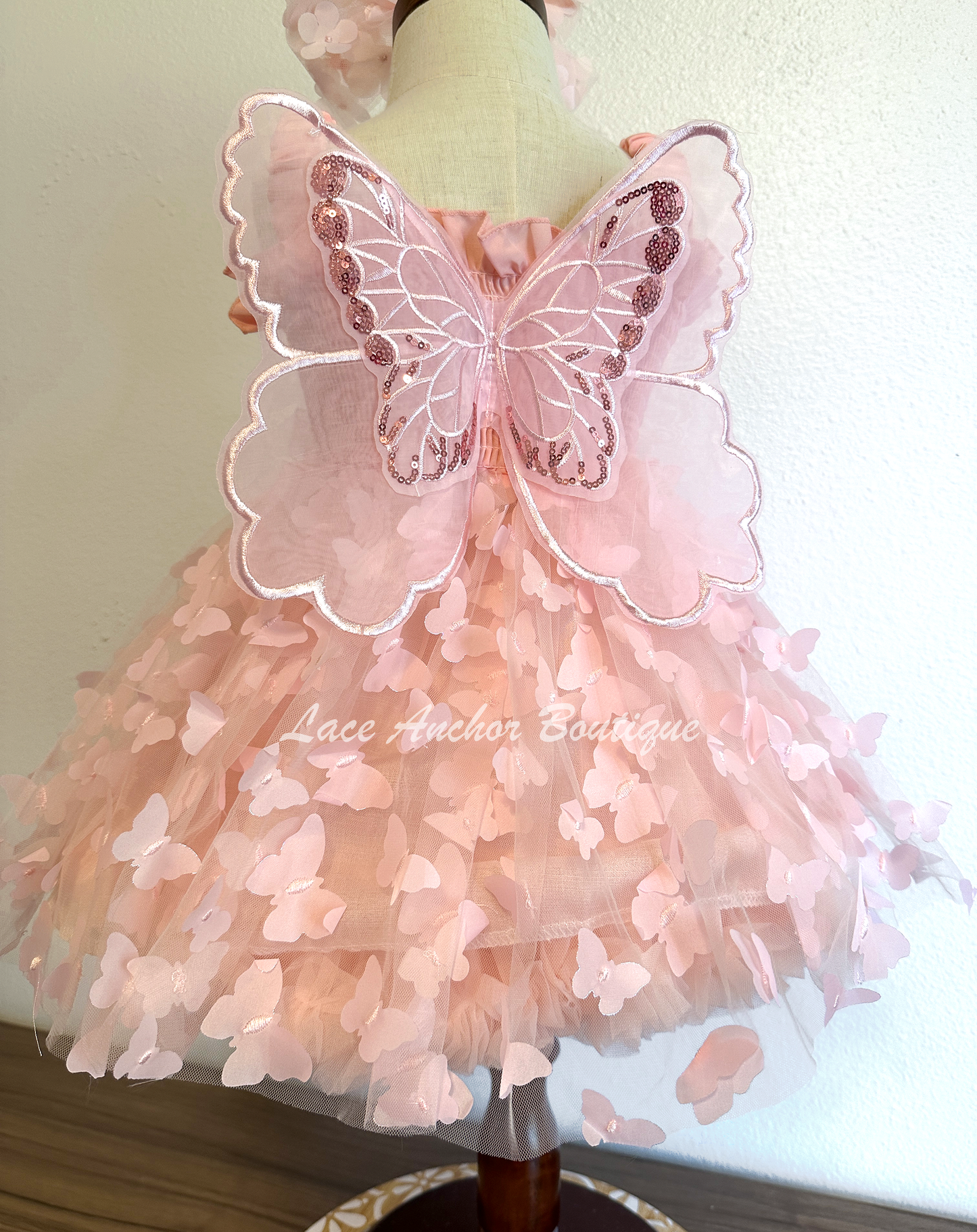 Light blush pale pink girls butterfly wing fairy dress in pink on model child toddler. Has butterflies all over skirt.