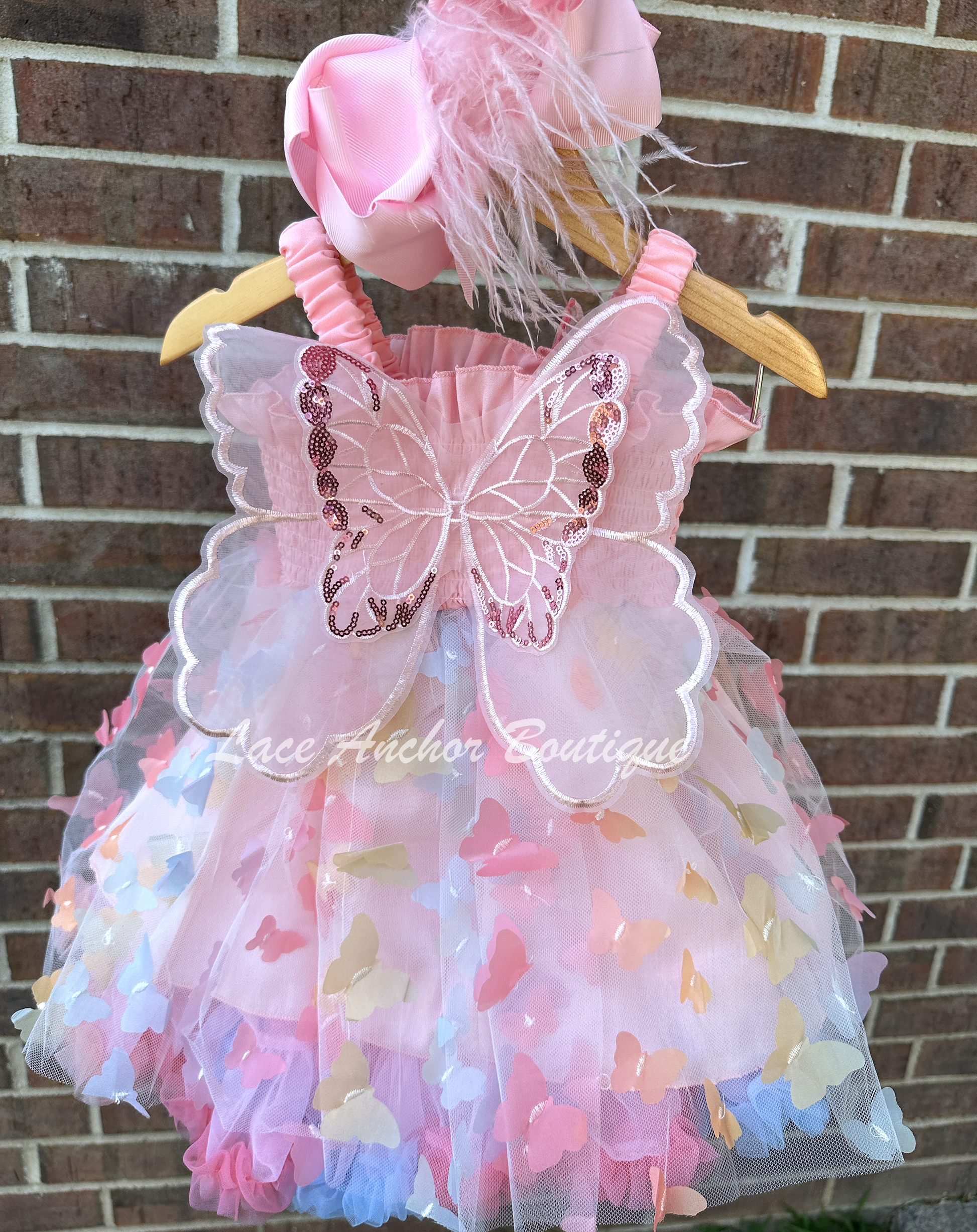 Light blush pale pink rainbow girls butterfly wing fairy dress in pink on model child toddler. Has butterflies all over skirt.