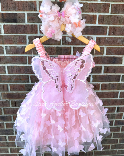 Light blush pale pink girls butterfly wing fairy dress in pink on model child toddler. Has butterflies all over skirt.