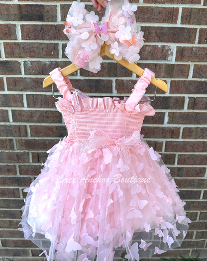 Light blush pale pink girls butterfly wing fairy dress in pink on model child toddler. Has butterflies all over skirt.