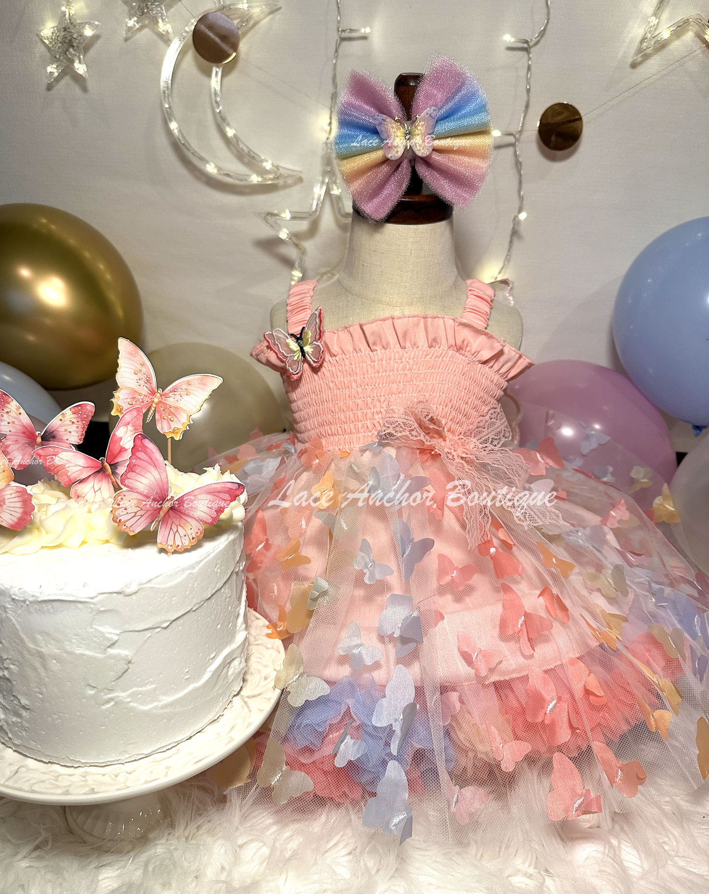 Light blush pale pink rainbow girls butterfly wing fairy dress in pink on model child toddler. Has butterflies all over skirt.