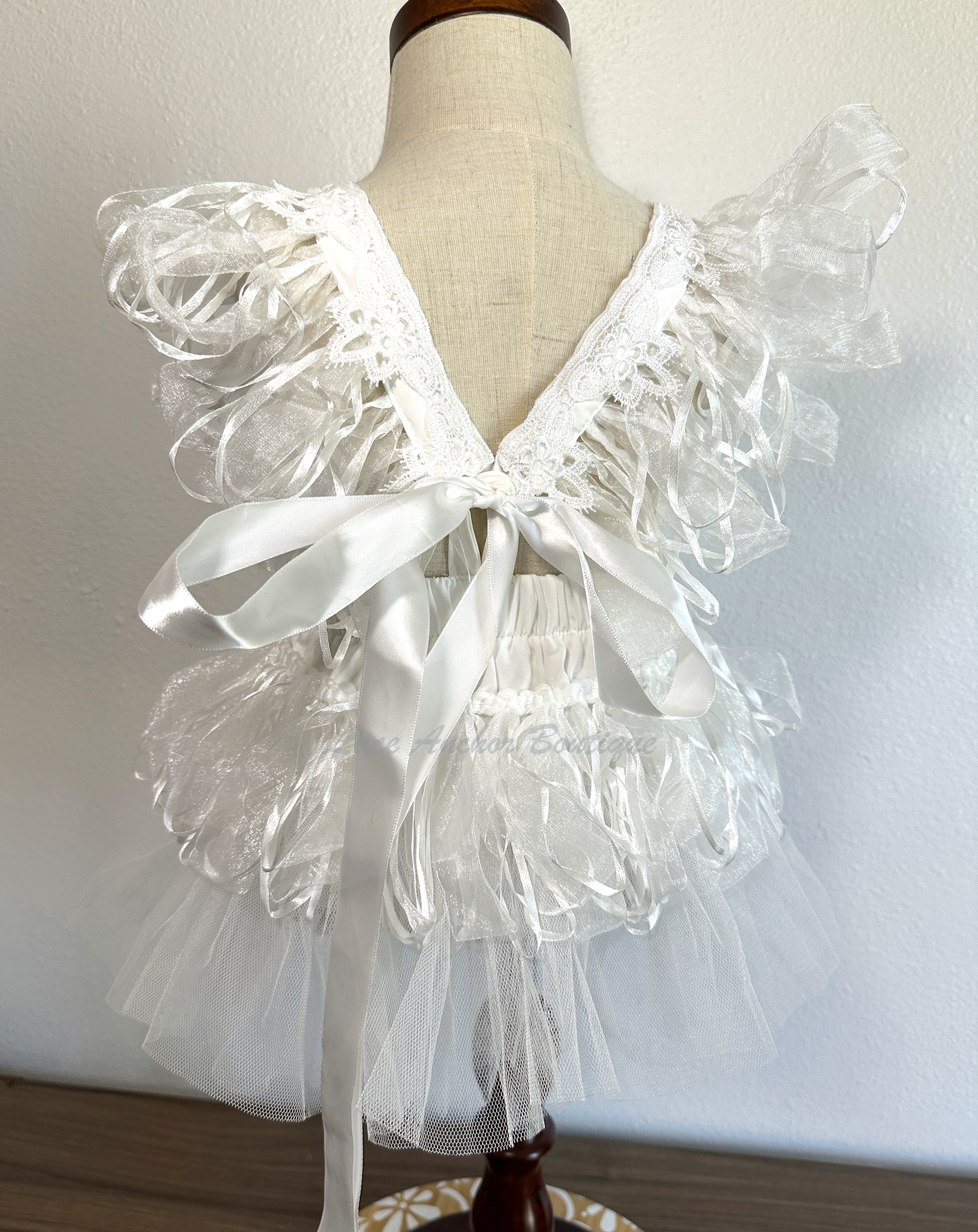 white baby girls romper with tulle half skirt, ribbon loop details, and embroidered floral applique across front