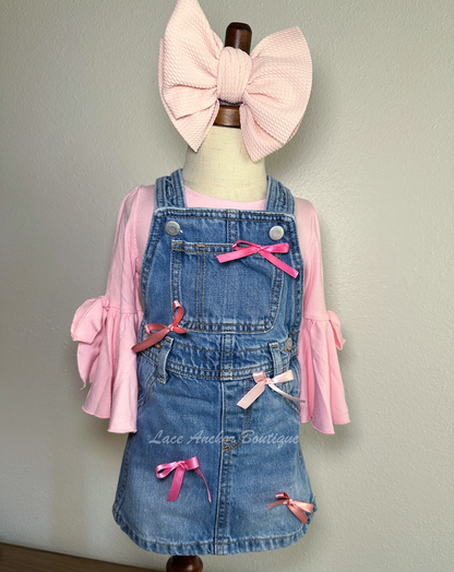 toddler girls blue denim overalls in a skirt style with multi colors of pink silky bows on a mannequin