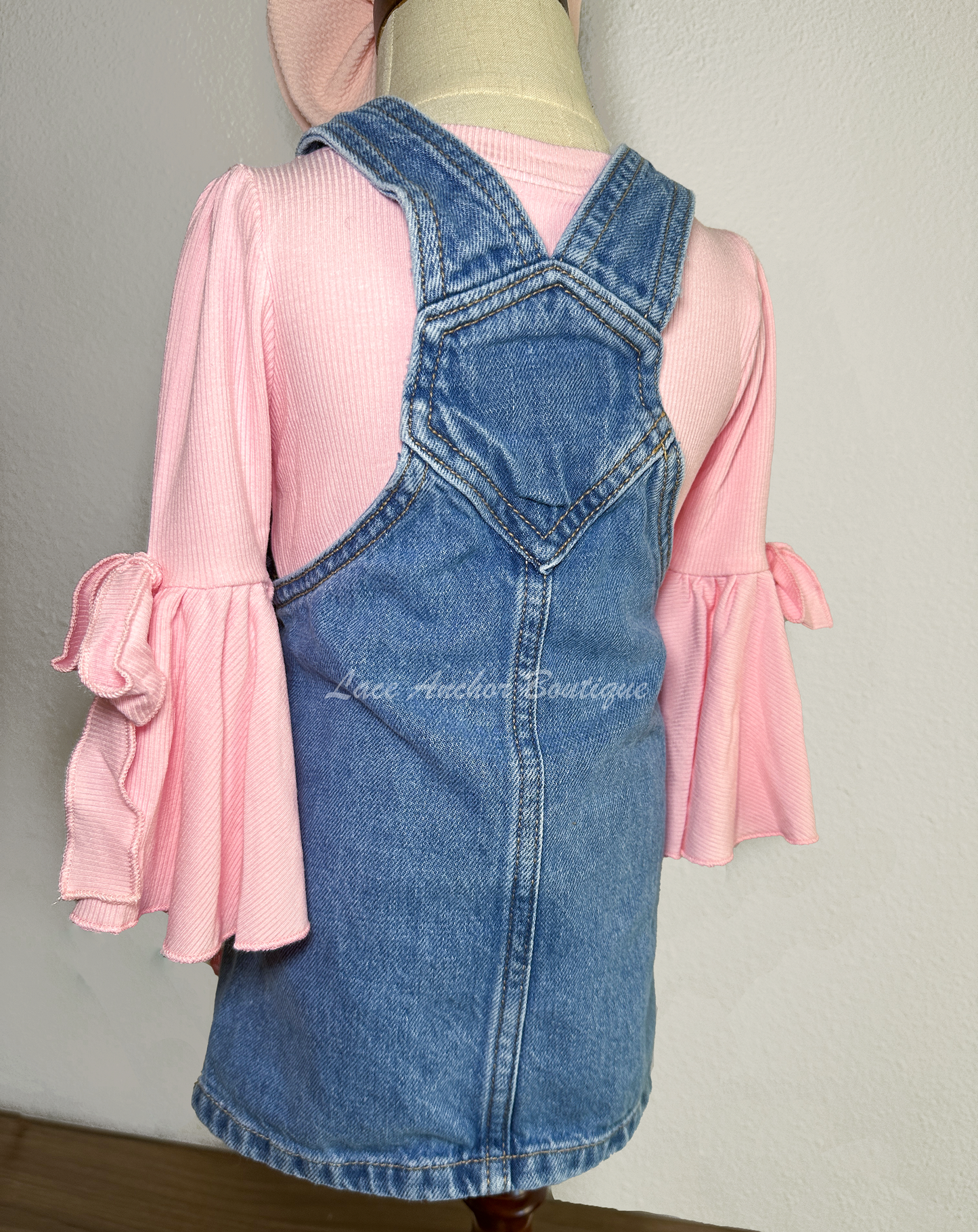 toddler girls blue denim overalls in a skirt style with multi colors of pink silky bows on a mannequin