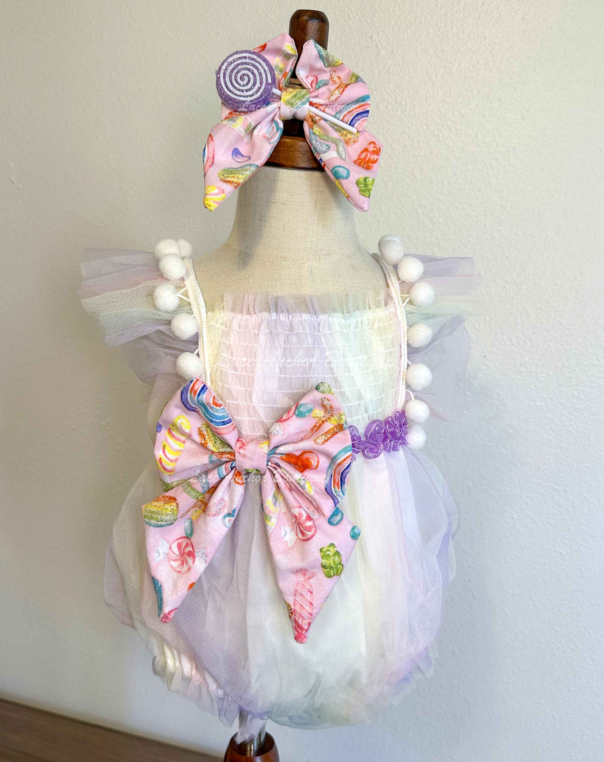 baby girls pastel lilac purple, yellow, blue, blue pink smocked tulle romper with candy themed big bow and matching hair bow with 3D sucker through it. Sweet One Candy Land Themed Outfit for birthday Photoshoots.