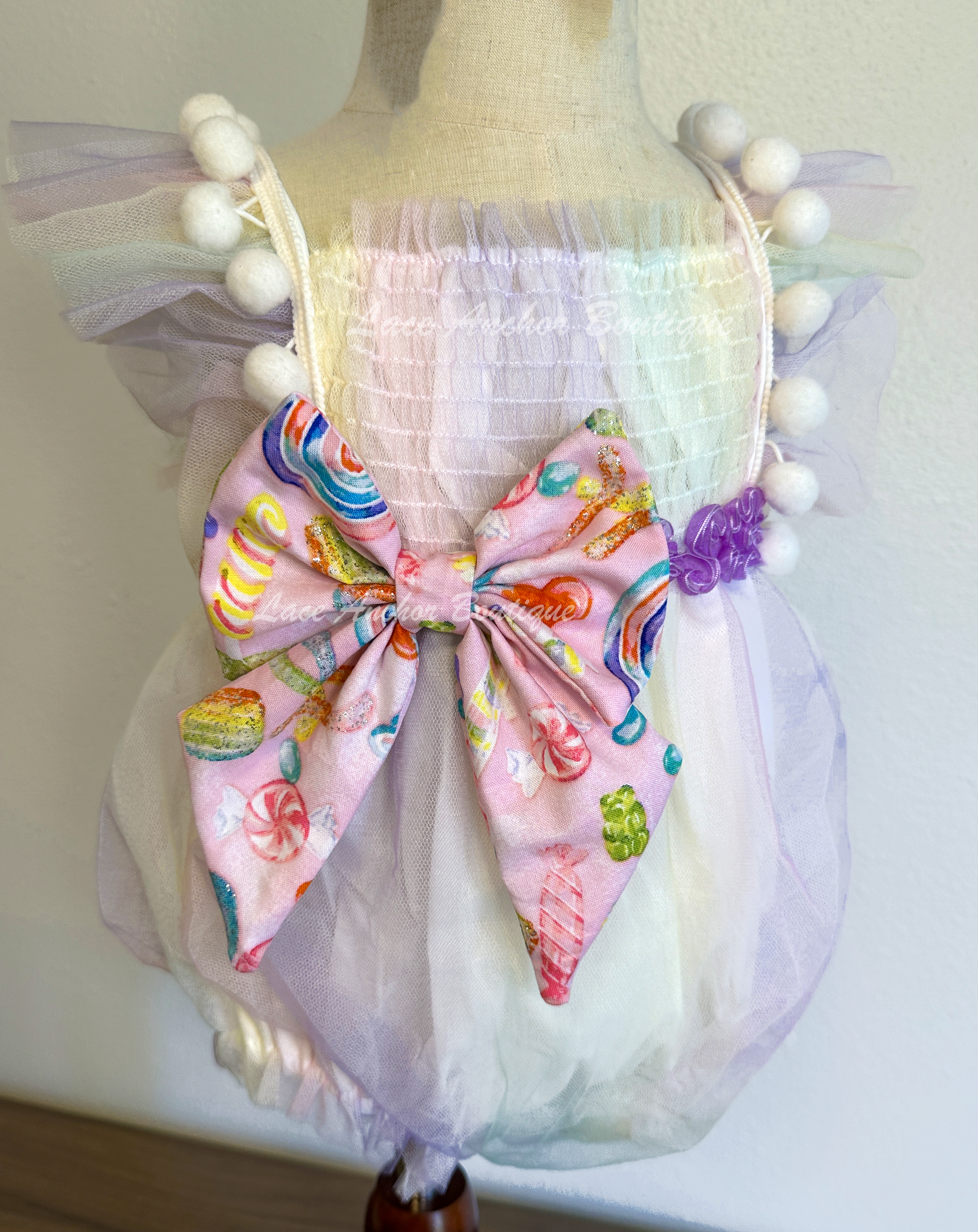 baby girls pastel lilac purple, yellow, blue, blue pink smocked tulle romper with candy themed big bow and matching hair bow with 3D sucker through it. Sweet One Candy Land Themed Outfit for birthday Photoshoots.