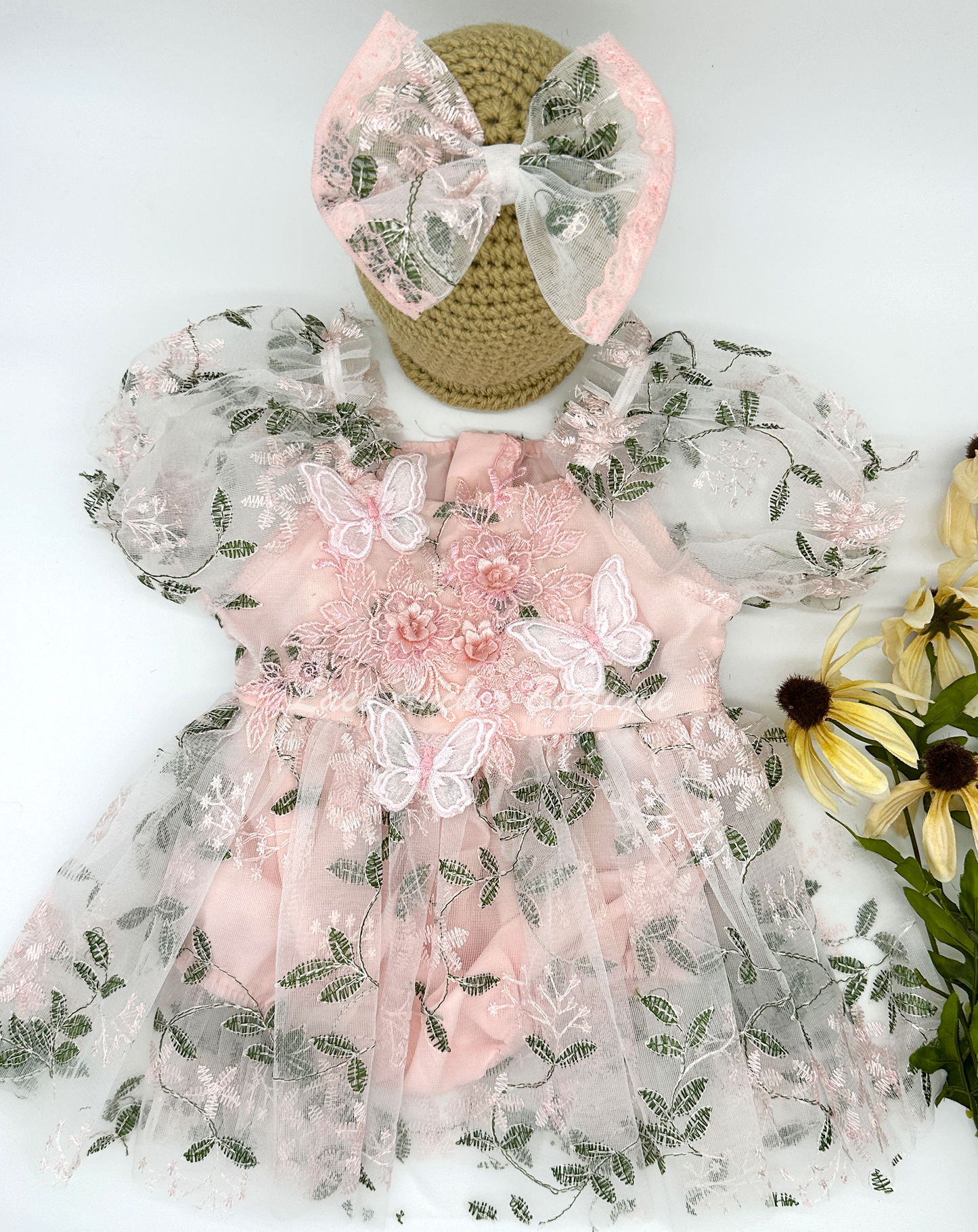 light blush pink embroidered floral print skirted baby girls romper with floral embroidered applique and butterflies with large tied bow on back and puffed short sleeves. Baby toddler flower girl dress.