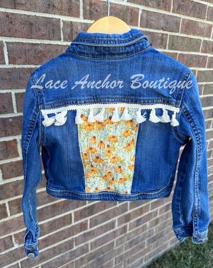 custom handmade upcycle toddler girls denim jacket with floral yellow sage sunflower fabric patch and ivory tassel trim.