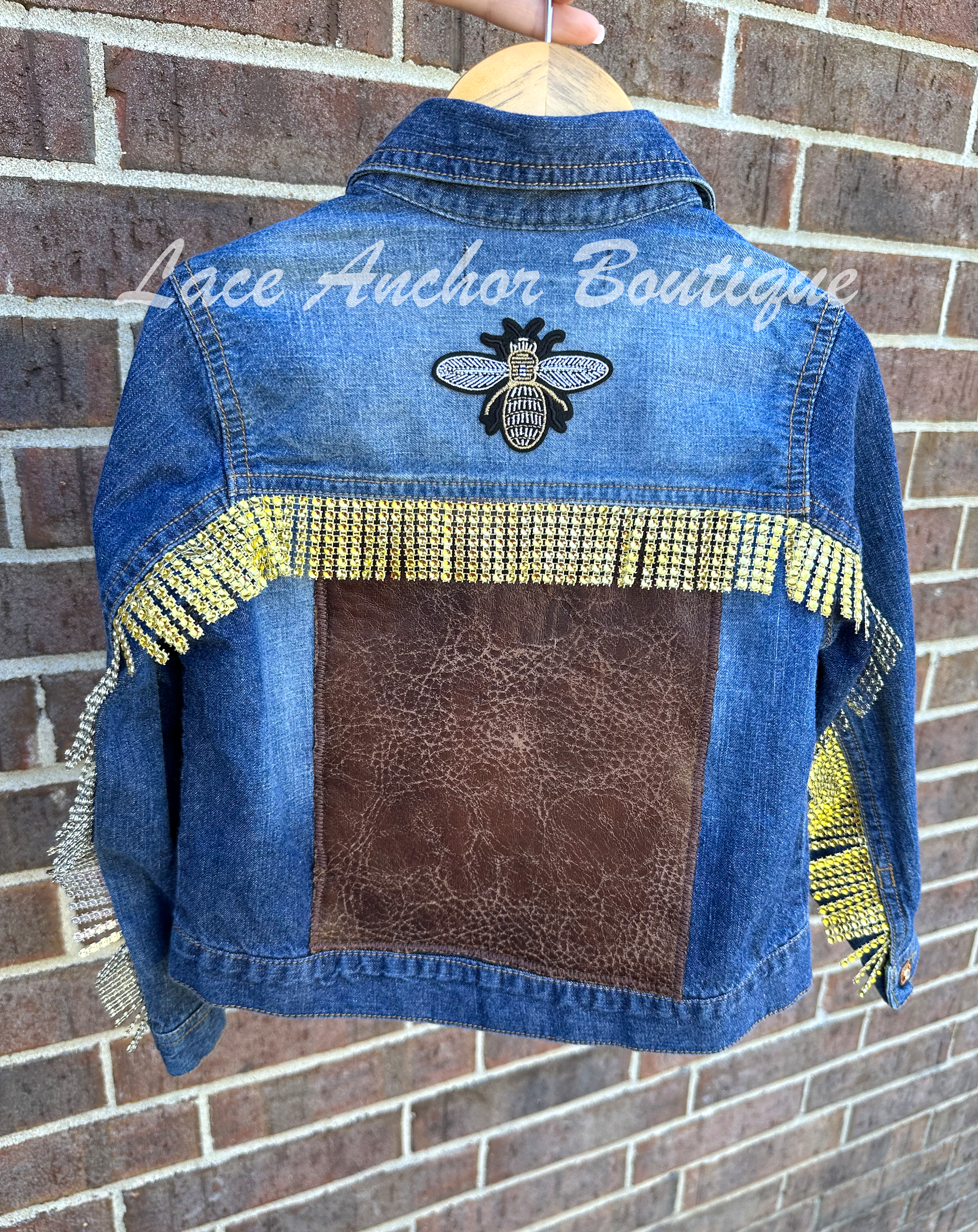 custom handmade upcycle toddler girls denim jacket with borwn distressed faux leather patch and gold rhinestone trim. Gold and black rhinestone bee patch and buttons.