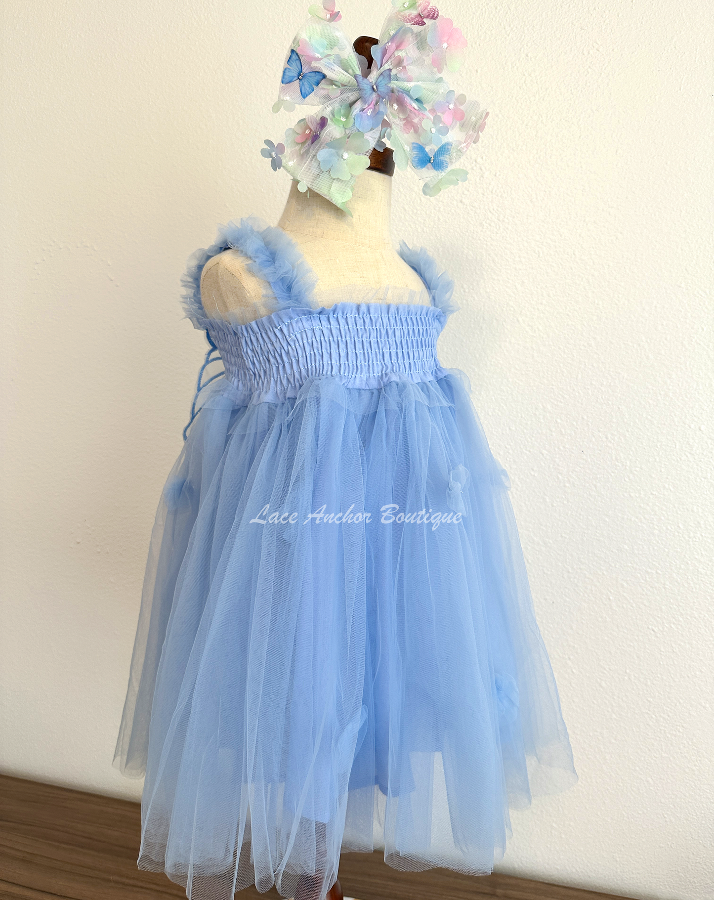 light blue tulle fairy girls dress with smocked top and tulle flowers on skirt. Attached butterfly wings and ruffled straps.