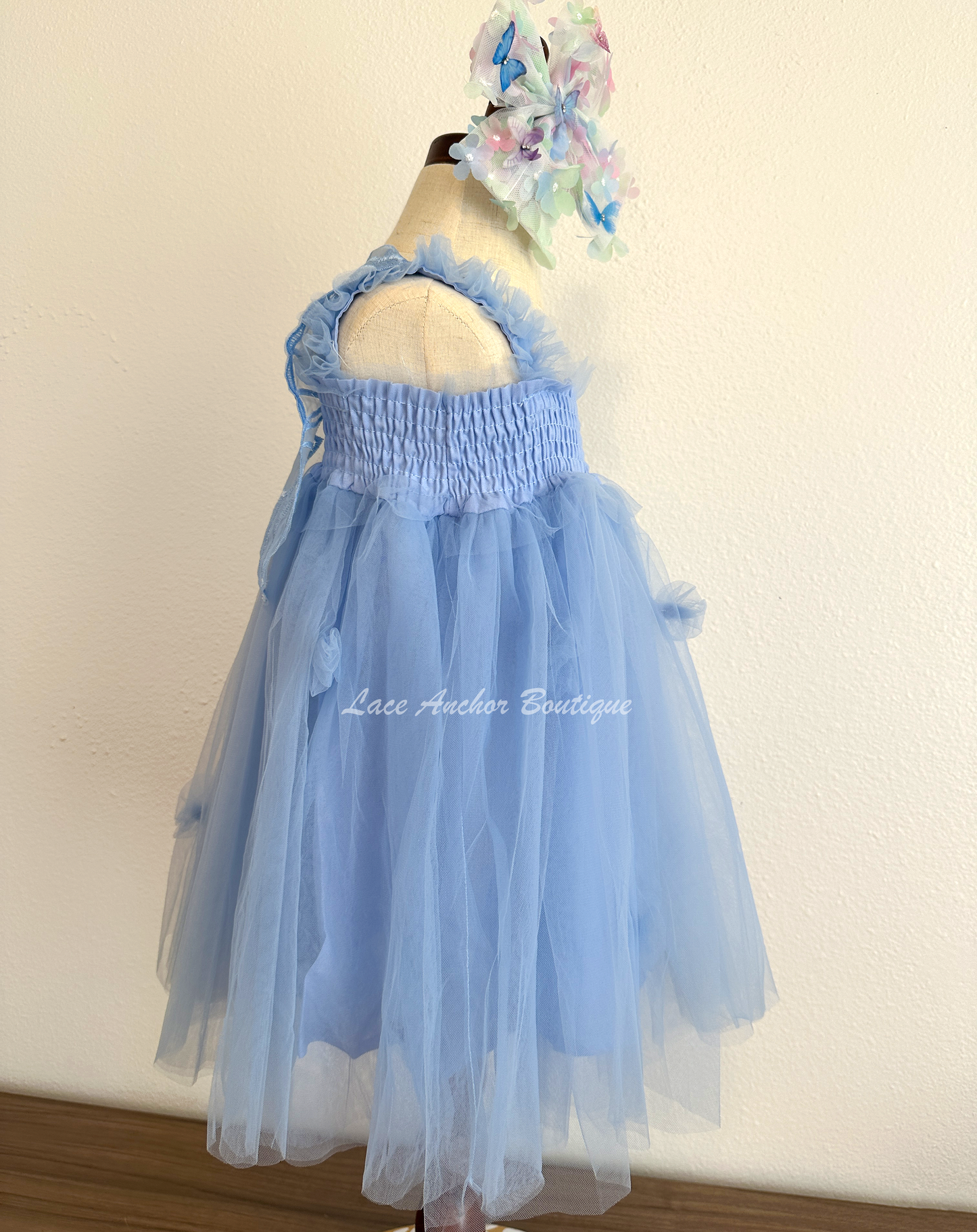 light blue tulle fairy girls dress with smocked top and tulle flowers on skirt. Attached butterfly wings and ruffled straps.