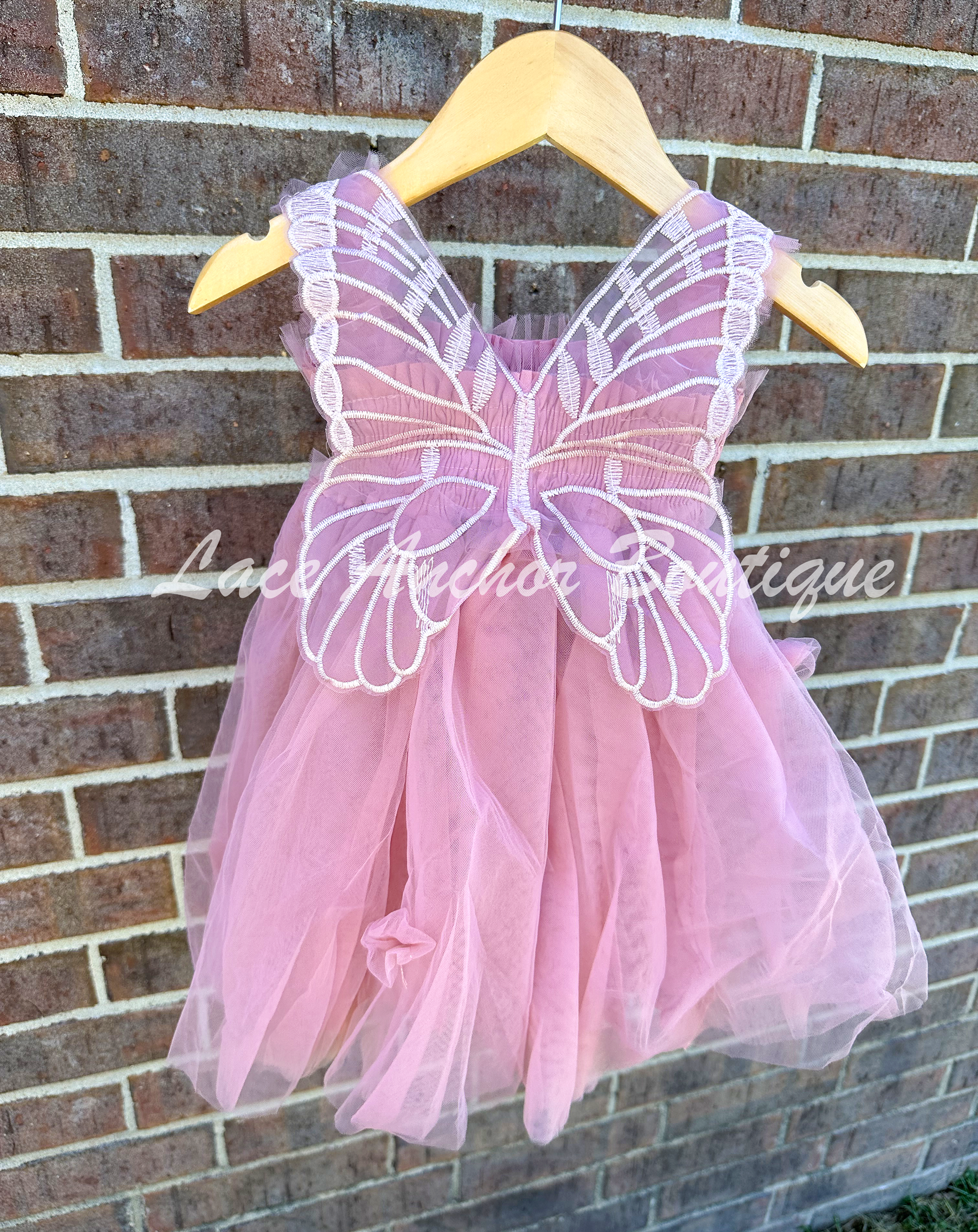 Mauve pink tulle fairy girls dress with smocked top and tulle flowers on skirt. Attached butterfly wings and ruffled straps. Worn by toddler model.