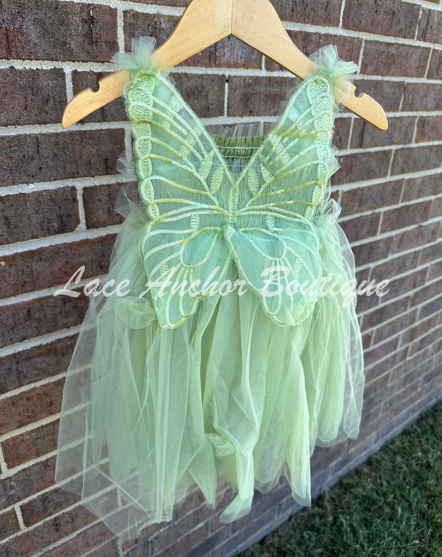 Sage Green tulle fairy girls dress with smocked top and tulle flowers on skirt. Attached butterfly wings and ruffled straps. Worn by toddler model.