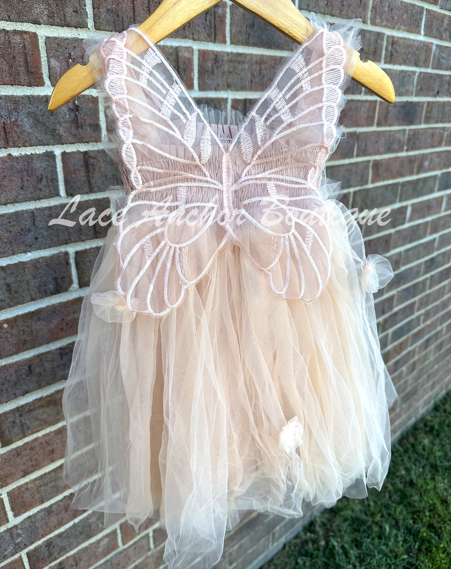 Champagne beige tulle fairy girls dress with smocked top and tulle flowers on skirt. Attached butterfly wings and ruffled straps. Worn by toddler model.