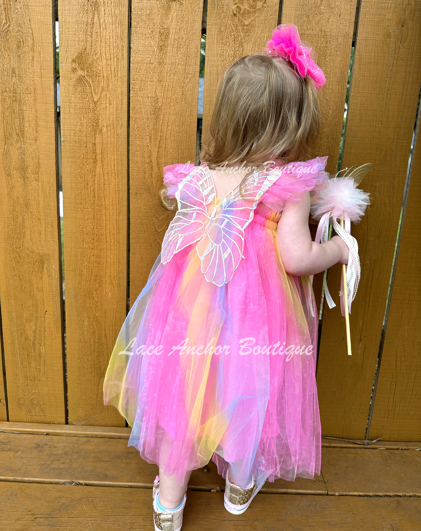 Neon rainbow fairy pink, blue, yellow, knee length tulle dress with iridescent butterfly wings attached on toddler model.
