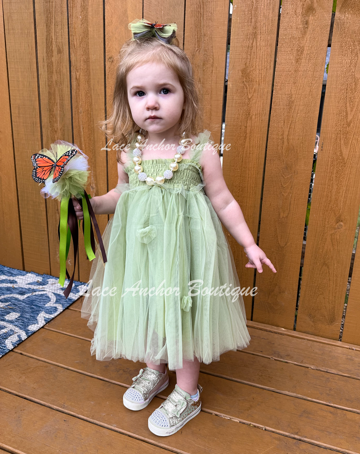 Sage Green tulle fairy girls dress with smocked top and tulle flowers on skirt. Attached butterfly wings and ruffled straps. Worn by toddler model.
