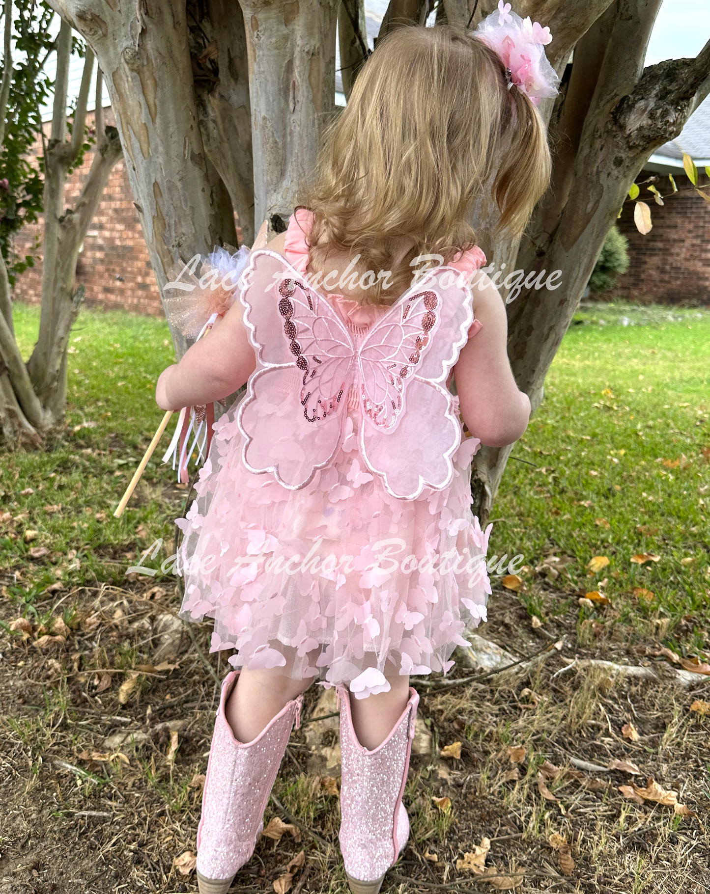 Light blush pale pink girls butterfly wing fairy dress in pink on model child toddler. Has butterflies all over skirt.