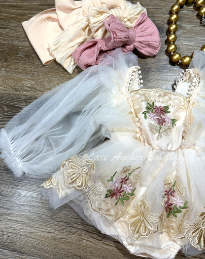 baby toddler girls flower girl romper with long puff sleeves, embroidered gold floral trim, skirt, and tied back. In blush light pink.