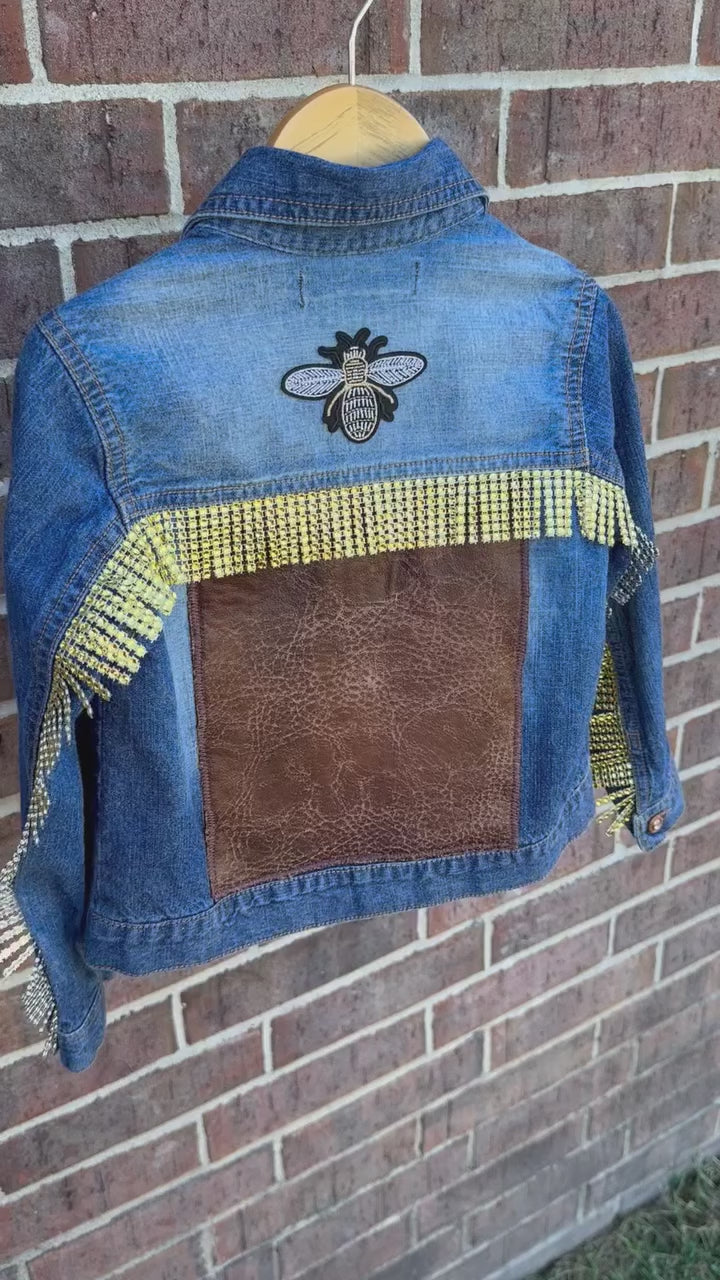 custom handmade upcycle toddler girls denim jacket with borwn distressed faux leather patch and gold rhinestone trim. Gold and black rhinestone bee patch and buttons.