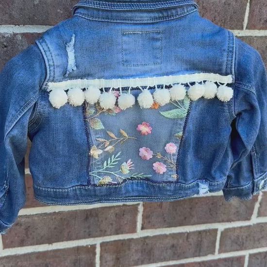 custom handmade upcycle toddler girls denim jacket with floral emboridered patch and ivory pom pom trim.