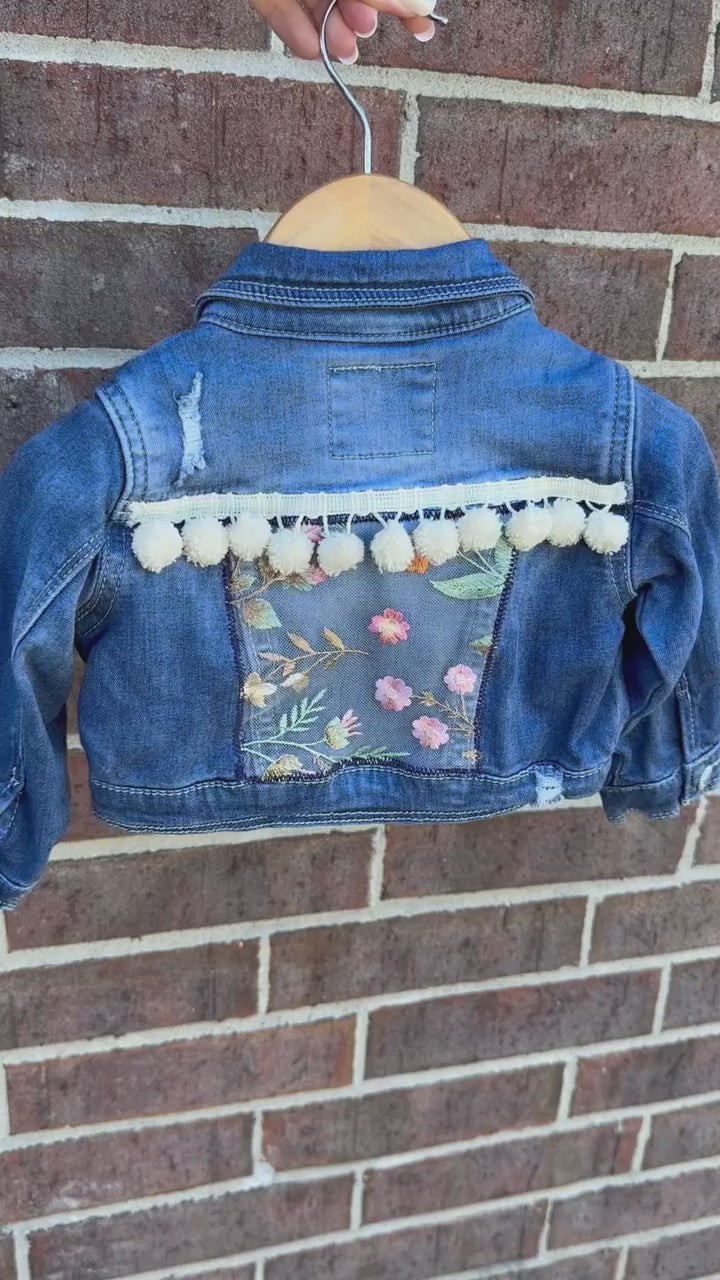 custom handmade upcycle toddler girls denim jacket with floral emboridered patch and ivory pom pom trim.